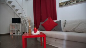 A modern living room with a red table, a sofa with red and grey cushions, a white TV stand, and a staircase. - Domus Claudiae's studio C-1 (Catania)
