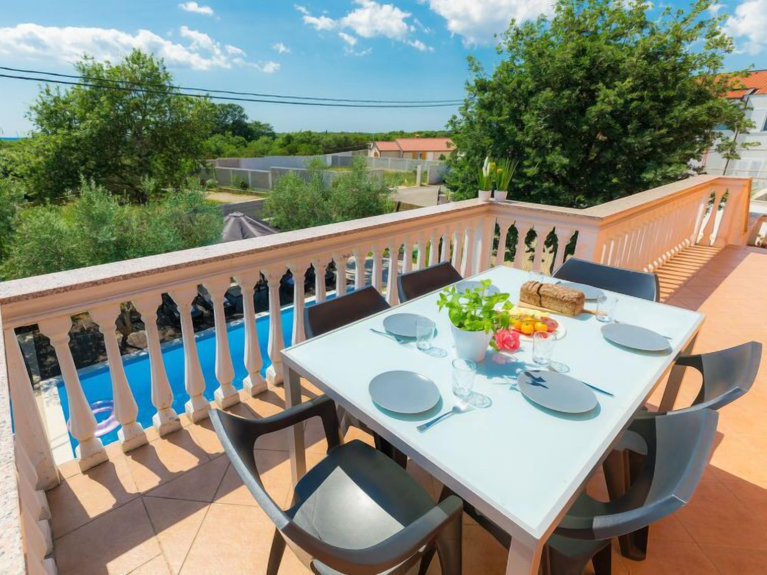 A dining table set for four with chairs, a pool in the background, and a view of a residential area.