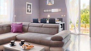 Uma sala de estar moderna com um sofá seccional, uma mesa de centro com doces e um espaço de jantar com mesa e cadeiras.