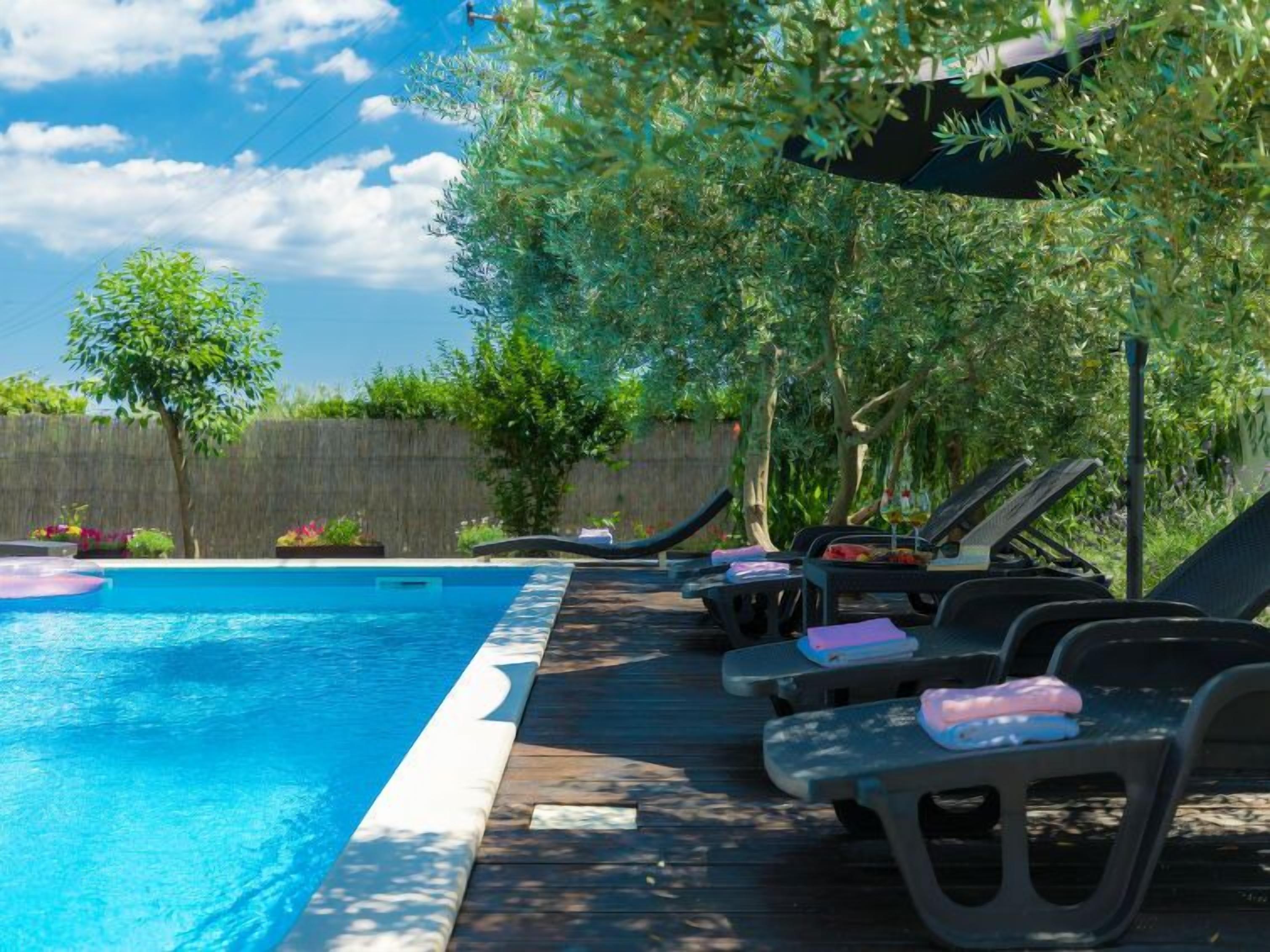 Ein Schwimmbecken mit Liegestühlen und Sonnenschirmen, umgeben von viel Grün.