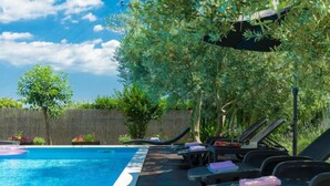 Piscina com espreguiçadeiras e guarda-sóis, rodeada por vegetação.