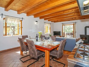 Een eetgedeelte met een houten tafel voor zes personen, omringd door comfortabele stoelen. Een televisie is aan de muur bevestigd, en er is een open haard zichtbaar op de achtergrond.
