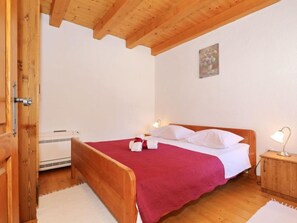Een slaapkamer met een houten bed, wit beddengoed, een rode deken en een klein nachtkastje met een lamp.