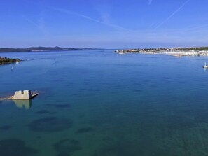 Een kustgezicht met een heldere blauwe zee, een klein eiland met gebouwen, en een steiger die het water in reikt.