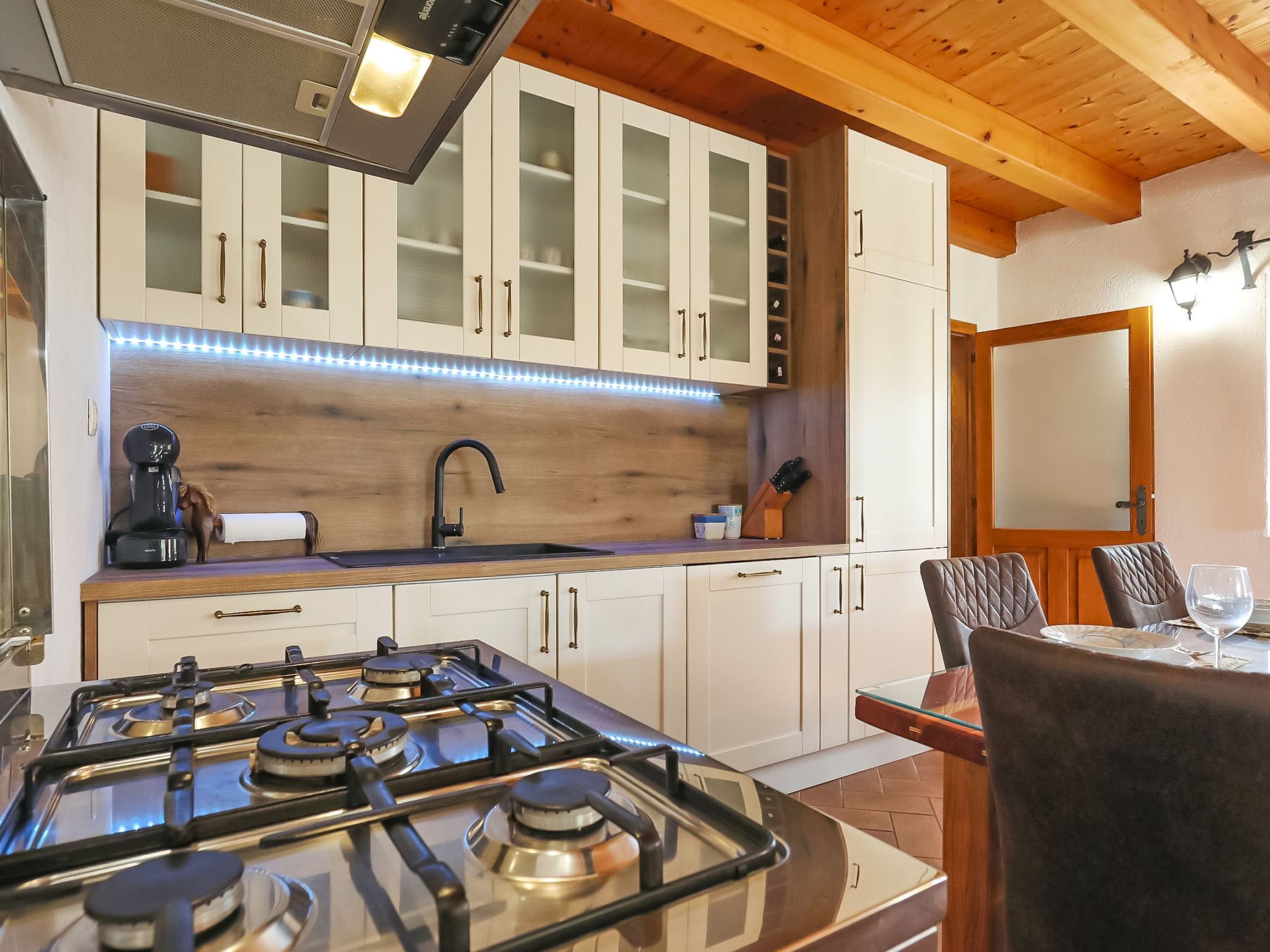 Een moderne keuken met een gasfornuis, houten kastjes en een eethoek met een tafel en stoelen.