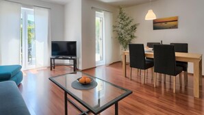A modern living room with a glass coffee table, a flat-screen TV, and a dining area with a wooden table and black chairs. - Vacation home Gojak by Interhome (Pula)
