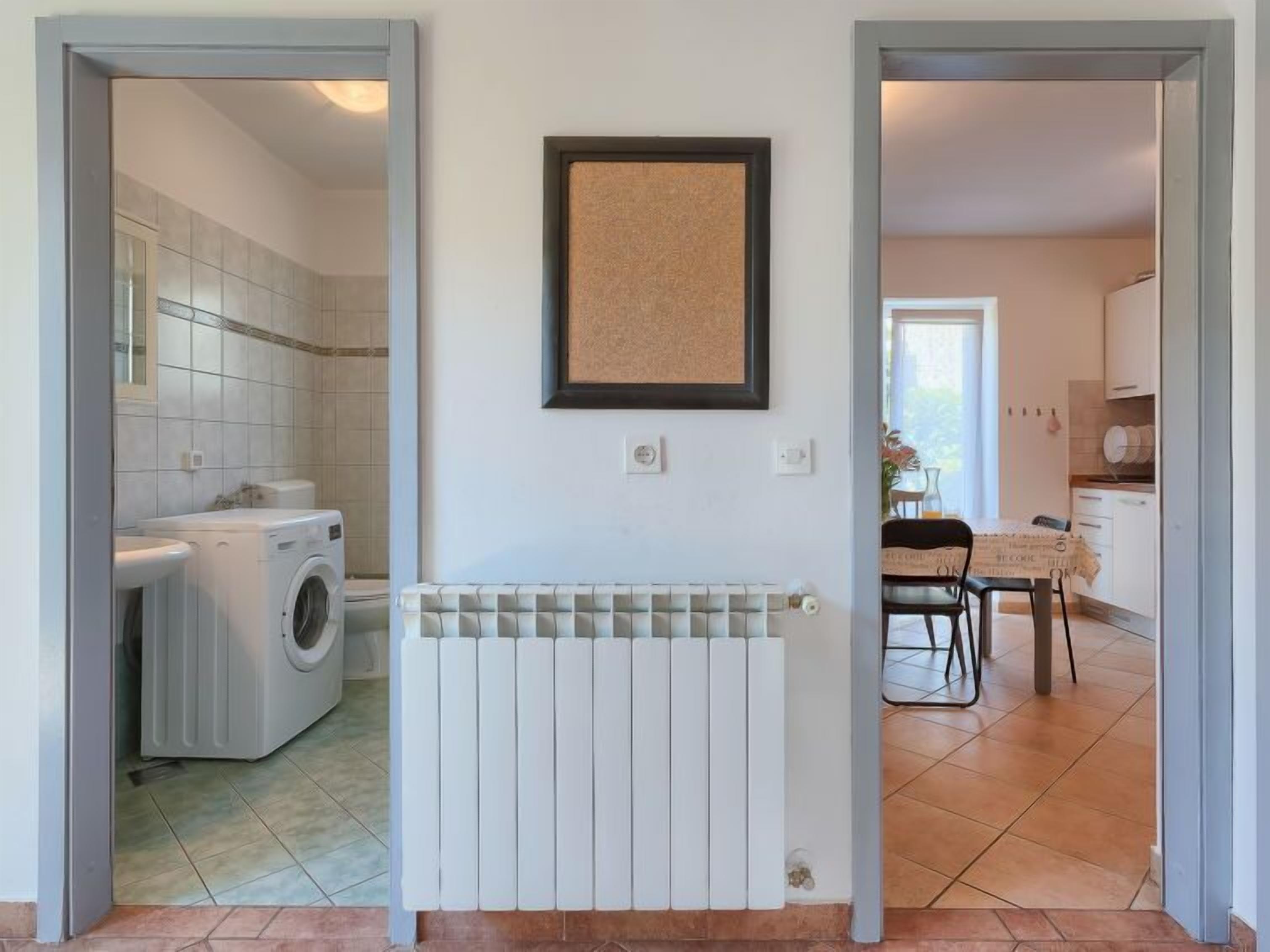 A laundry area with a washing machine, a radiator, and a framed picture on the wall.