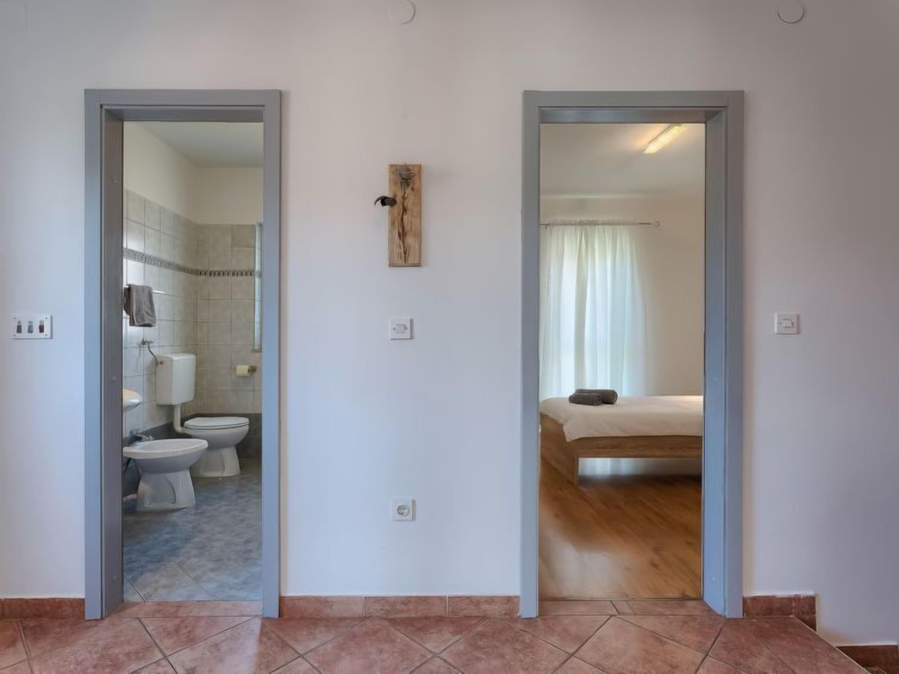 Ein Zimmer mit einem Bett, einem Badezimmer mit Toilette und Dusche sowie einem Spiegel, der das Zimmer reflektiert.