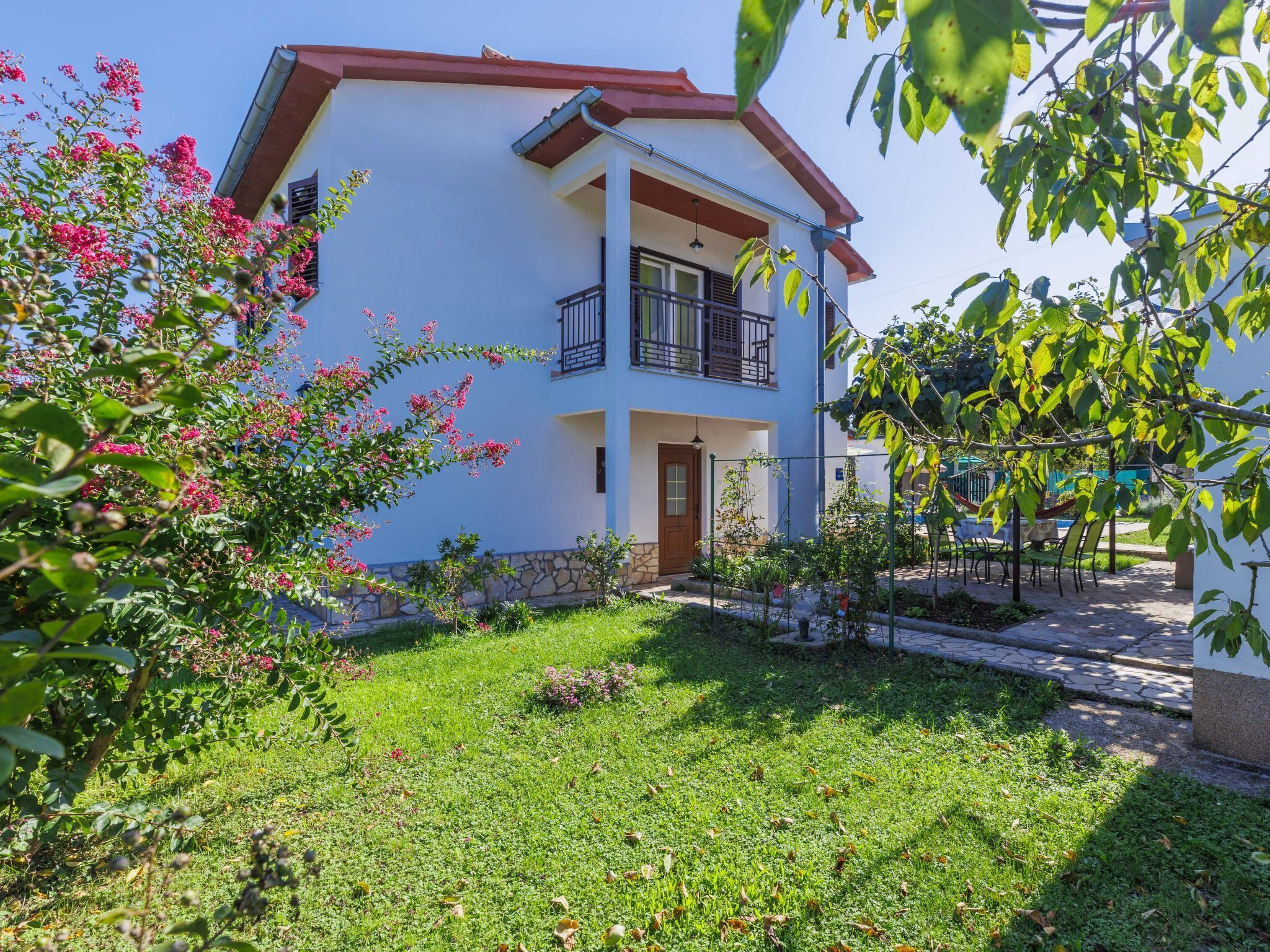 A two-story building with a balcony, surrounded by a well-maintained garden with flowering plants.