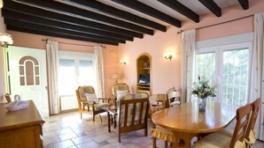 A dining area with a wooden table and chairs, a bookshelf, and a window with curtains. - Vacation home Amber by Interhome (Calpe/Calp)