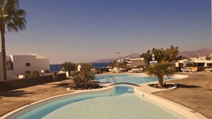 Zona de piscina con vista despejada al mar, rodeada de palmeras y edificios modernos.