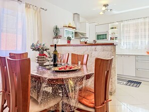 Un coin repas avec une table ronde, des chaises, une bouteille de vin et une assiette de nourriture.