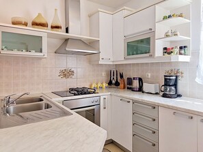 Une cuisine moderne avec des meubles blancs, une cuisinière à gaz, un évier et une machine à café.