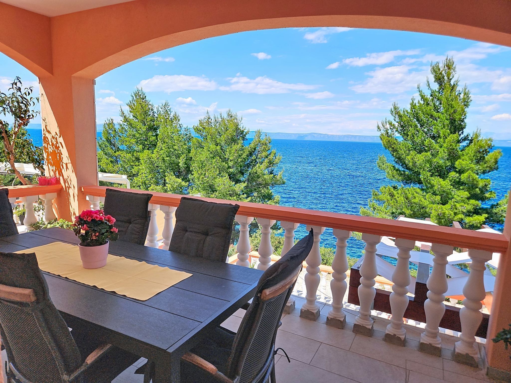 Ein Balkon mit Tisch und Stühlen mit Blick auf ein Gewässer und Grünflächen.