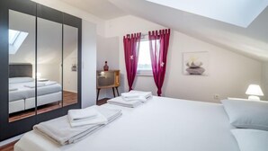 A modern bedroom with a skylight, a large bed with neatly folded white towels, a television on a small table, and a window with red curtains.