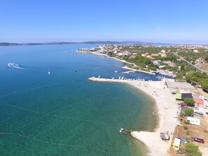 Eine Luftaufnahme einer Küstenstadt mit klarem, blauem Wasser, einem Sandstrand und einer Marina mit Booten.