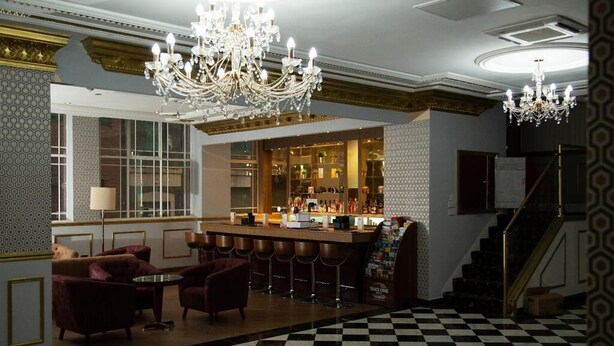 A bar area with a checkered floor, bar stools, a chandelier, and a bar counter with bottles. - The Ladbrooke Hotel (Birmingham)