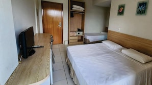 A hotel room with a wooden desk, a bed with white bedding, a wardrobe, and a small table with a chair. - Golden Dolphin Express (Caldas Novas)