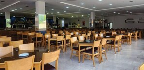 Un comedor amplio con varias mesas y sillas, una barra al fondo y un diseño moderno y limpio.