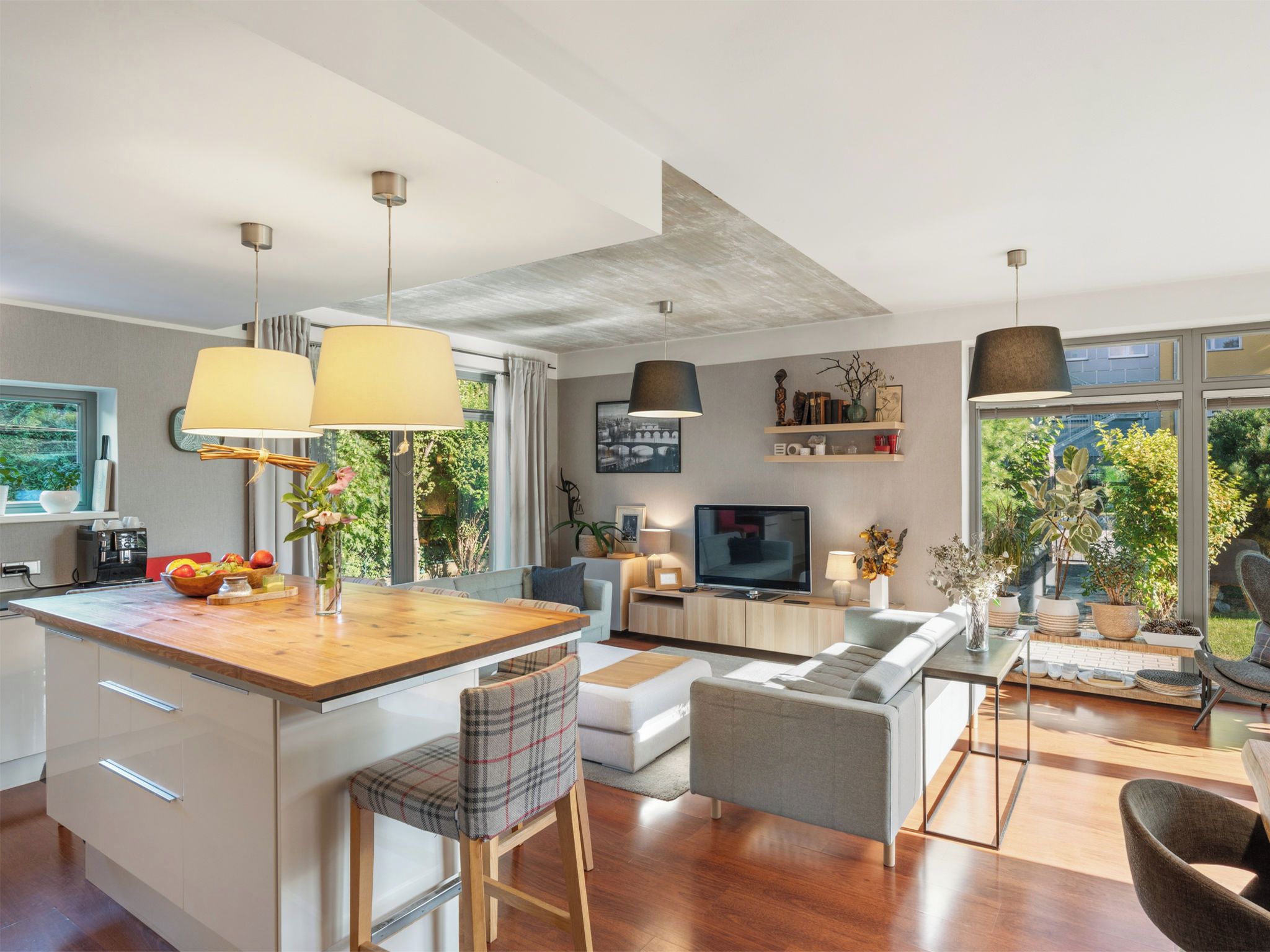 Une cuisine moderne avec un îlot central, un coin repas comprenant un canapé et des chaises, et un salon avec un téléviseur et des objets décoratifs.