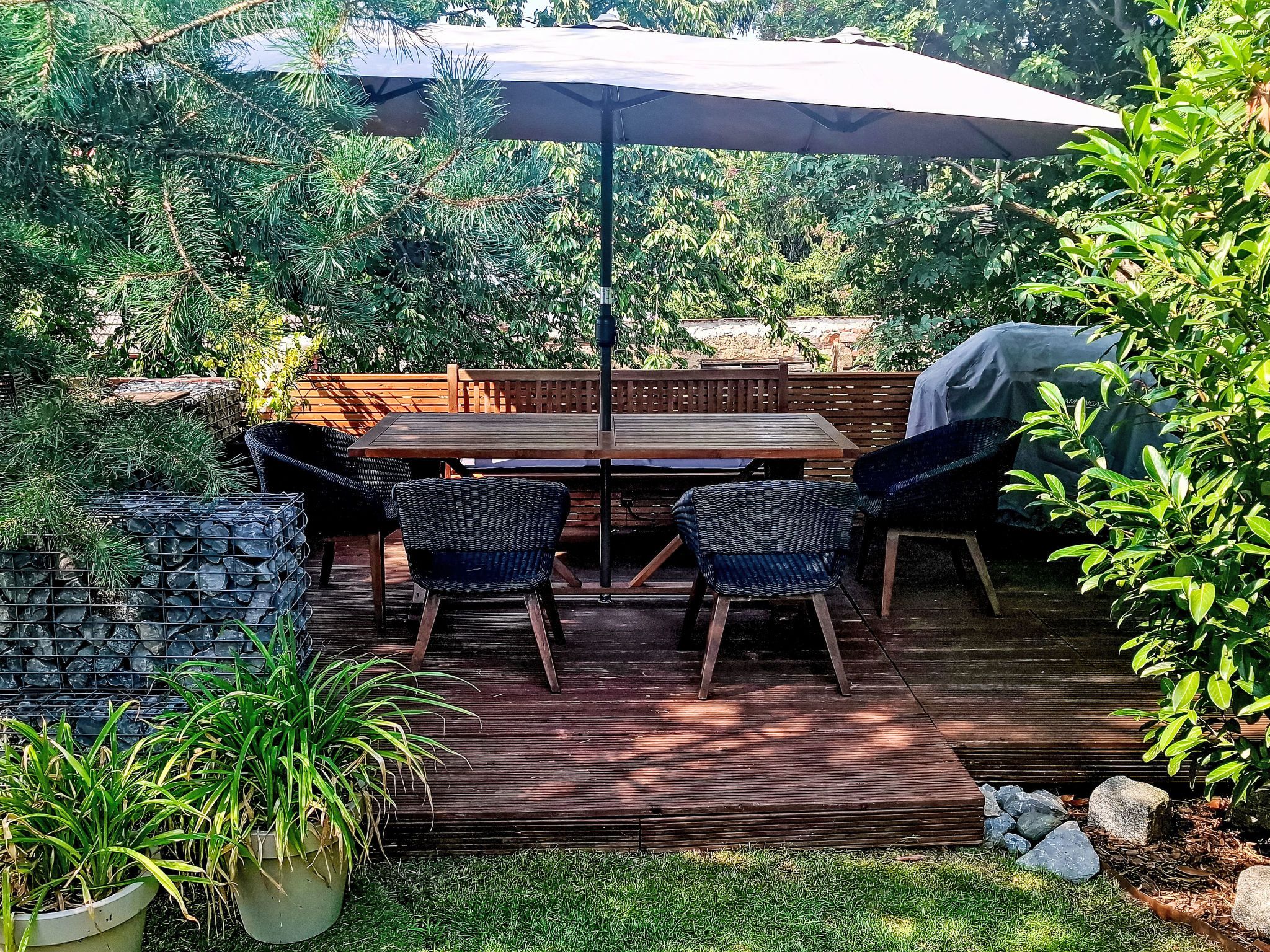 An outdoor patio with a wooden deck, a table, four chairs, and a large umbrella.