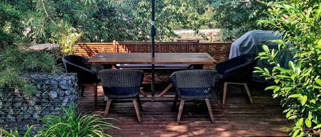 Un patio al aire libre con cubierta de madera, una mesa, cuatro sillas y una sombrilla grande.