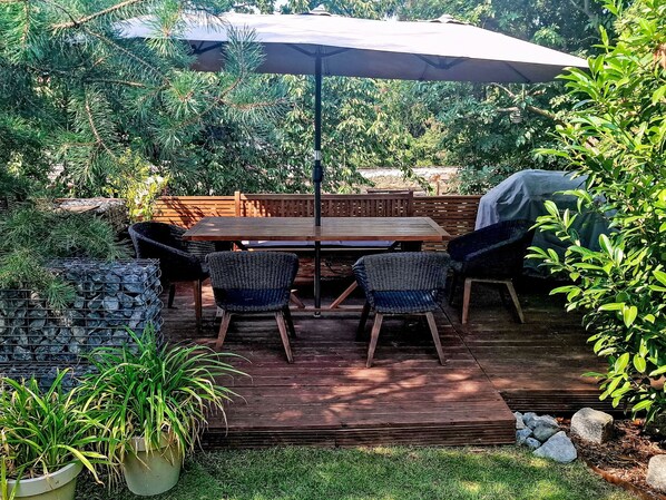 An outdoor patio with a wooden deck, a table, four chairs, and a large umbrella.