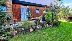 A modern house with a wooden facade, a blue door, and a well-maintained garden with various plants and a lawn.