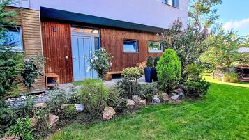 A modern house with a wooden facade, a blue door, and a well-maintained garden with various plants and a lawn.