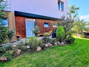 A modern house with a wooden facade, a blue door, and a well-maintained garden with various plants and a lawn.