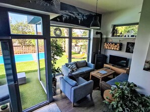 A modern living room with large windows, a fireplace, a TV, and a pool view.