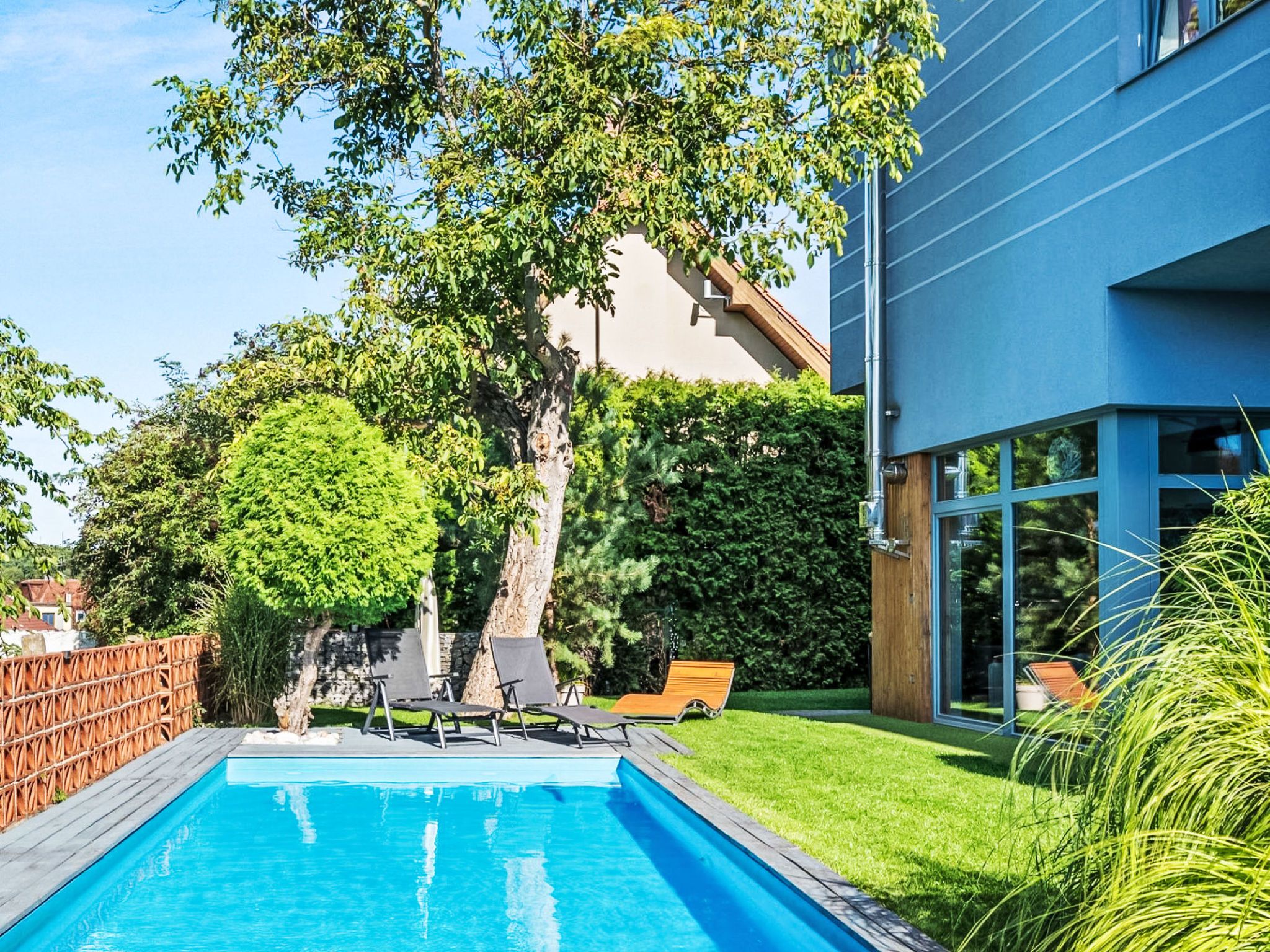 A swimming pool with lounge chairs, a tree, and a modern building.