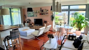 A modern living room with a sofa, dining table, and chairs, a TV, and a large window with a view of greenery. - Řeporyje by Interhome (Reporyje)