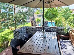 An outdoor patio with a wooden table and chairs, a stone wall, and a view of a swimming pool. - Řeporyje by Interhome (Reporyje)