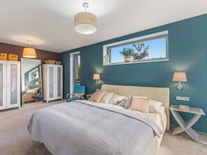 A bedroom with a large bed, a wardrobe, a chair, a bedside table, and a window with a view of trees. - Řeporyje by Interhome (Reporyje)