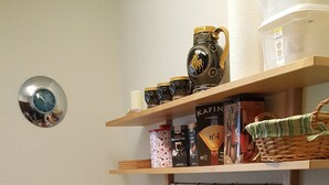 Eine kleine Küche mit einem runden Tisch, zwei Stühlen, einer Küchenzeile mit Geschirr und einem Hängegestell mit Küchenutensilien.