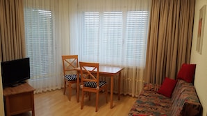 Ein Wohnzimmer mit Fernseher auf einem Schrank, einem Holztisch mit Stühlen und einer Couch mit gemusterten Kissen.