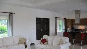 Ein modernes Wohnzimmer mit zwei weißen Sofas, einem Couchtisch und einer Küchenzeile mit roten Barhocker.