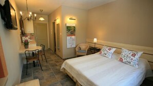 Ein Hotelzimmer mit einem Bett, einem Schreibtisch, einem Sessel, einem kleinen Tisch, einer Topfpflanze und einem an der Wand befestigten Fernseher.