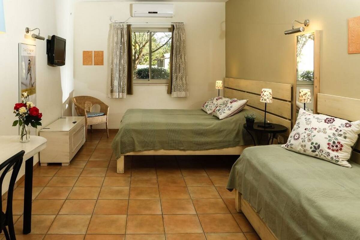 A small, tidy room with two beds, a desk, a chair, and a window with curtains.
