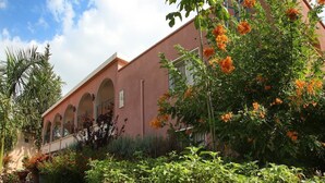 Ein Gebäude mit einer rosafarbenen Fassade, gebogenen Balkonen und einem Garten mit orangefarbenen Blumen.