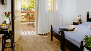 Ein Schlafzimmer mit Bett, Schreibtisch mit Stuhl, Fenster mit Vorhängen und Blick ins Freie.