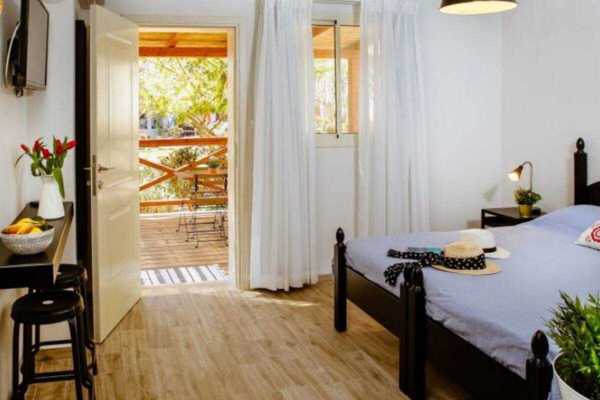 A bedroom with a bed, a desk with a chair, a window with curtains, and a view of an outdoor area.