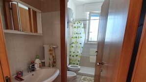 Un baño con un lavamanos, dos inodoros, una cortina de ducha y una puerta de madera.