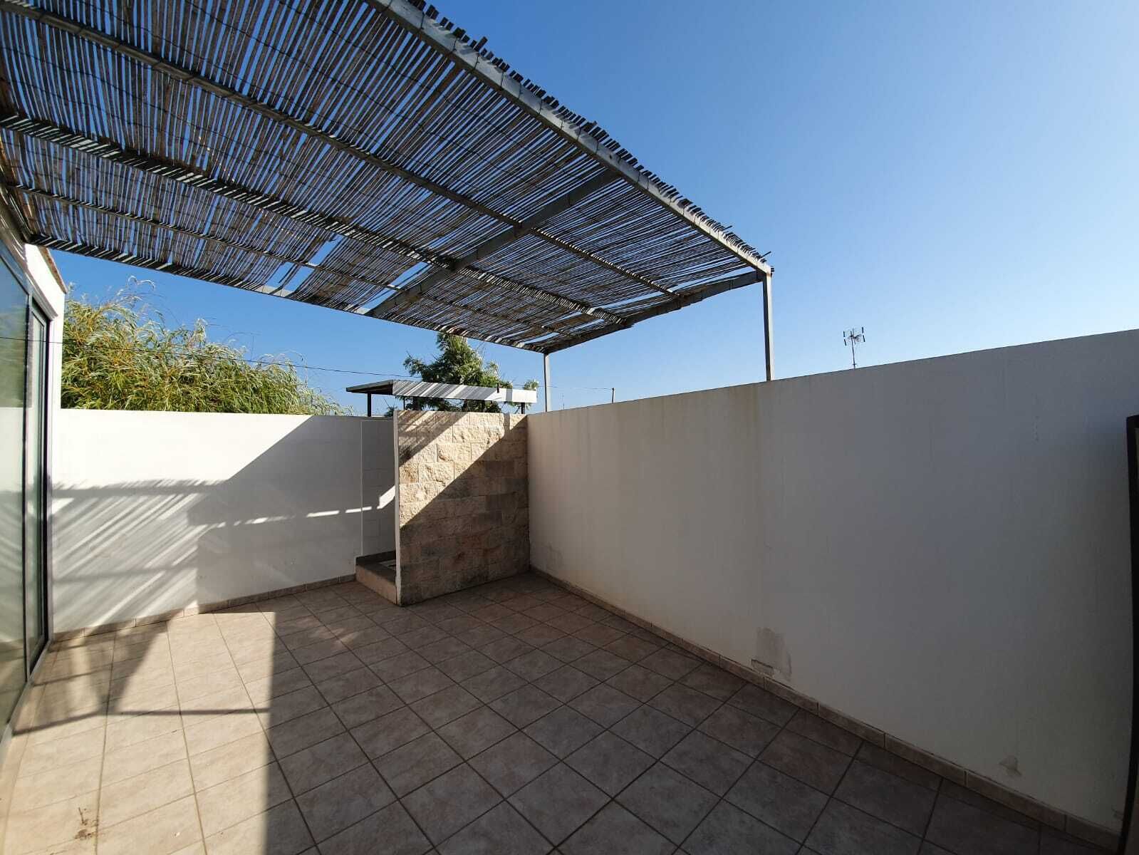 Un espace extérieur abrité, doté d’un sol carrelé et d’une structure de toit en métal.