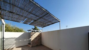 Un espacio al aire libre cubierto, con suelo de baldosas y estructura de techo metálica.
