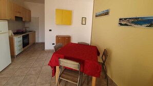 Una cocina compacta con armarios de madera, una pequeña mesa de comedor con mantel rojo y una silla.