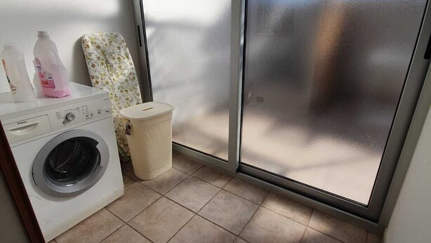 Un espacio pequeño para lavandería con lavadora, tendedero y cubo de basura.