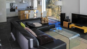 Una sala de estar moderna con un sofá de cuero negro, una mesa de centro de vidrio y un televisor de pantalla plana.
