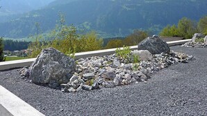 Un área pavimentada con rocas grandes y vegetación escasa, con vistas a un paisaje montañoso de picos nevados.